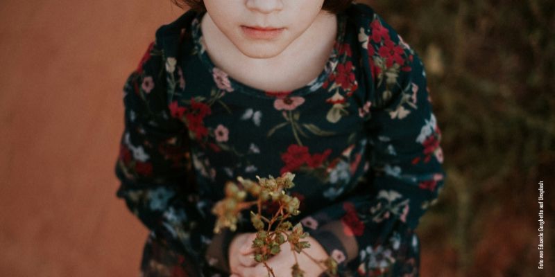 Ein Kind in einem Blumenkleid schaut nach oben. Die Augen sind abgeschnitten. Foto von Eduardo Gorghetto auf Unsplash